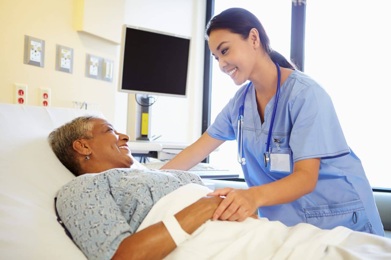 A nurse checking in on an older woman in a hospital room.