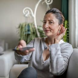 Adult woman with hearing aid watching television and adjusting her device.