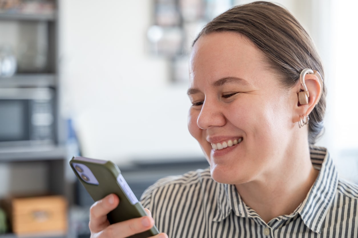 Woman with hearing aid smiling at her phone.