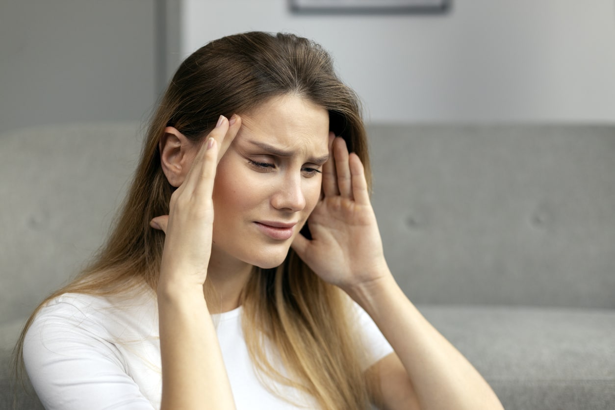 Woman with tinnitus, looking upset and holding her head.