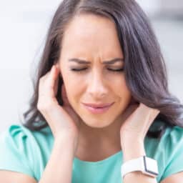 Young woman holding her ears because of tinnitus