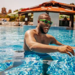 Young man having fun at public swimming pool in water on his vacation