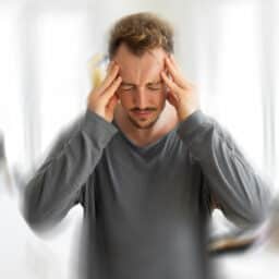 Man with tinnitus holding his head, blurred effect around him