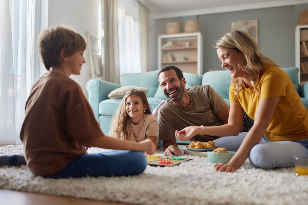Happy parents and their kids playing a game on carpet at home.
