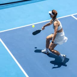 High-angle view of a female pickleball player hitting a backhand shot outdoors.