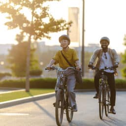 Two people enjoying a leisurely bike ride through the city. The sun shines brightly, casting a warm glow over the scene, and highlighting the joy of outdoor activities.