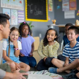 Teach sitting on the floor with his students, telling a story.