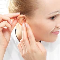 Young woman puts on a hearing aid.