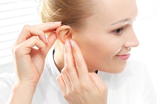 Young woman puts on a hearing aid.
