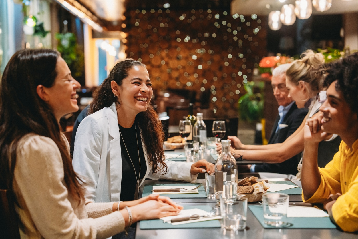 Group of friends laughing and enjoying dinner together at a restaurant, celebrating and having fun.